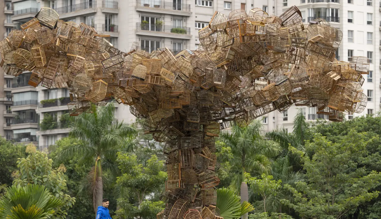 <p>Seorang pria berjalan melewati instalasi seni karya seniman Brasil Eduardo Srur yang menggambarkan sebuah pohon terbuat dari ratusan sangkar burung sitaan polisi lingkungan dari pedagang hewan di Taman Parque do Povo, Sao Paulo, Brasil, 6 Mei 2022. Menurut Eduardo Srur, pameran "Vida Livre" atau "Kehidupan Bebas" bertujuan memprovokasi masyarakat agar memikirkan kembali budaya hewan yang terperangkap untuk hiburan manusia. (AP Photo/Andre Penner)</p>