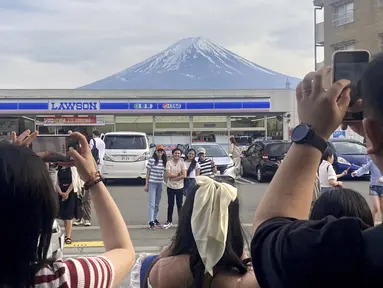 Para pengunjung mengambil foto di depan toko serba ada di kota Fujikawaguchiko, prefektur Yamanashi, Jepang, dengan latar belakang Gunung Fuji pada tanggal 28 April 2024. (Kyodo News via AP)