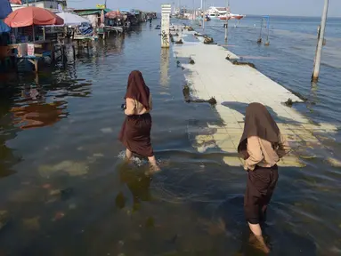 Siswi melintasi banjir rob di Pelabuhan Kali Adem, Muara Angke Jakarta, Rabu (5/1/2022). Menurut BMKG, adanya fase bulan baru yang bersamaan dengan masa Perigee (jarak terdekat bulan bumi) menyebabkan peningkatan signifikan ketinggian pasang air laut mencapai maksimum. (merdeka.com/Imam Buhori)