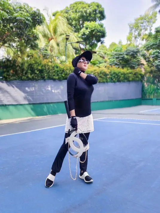 Pilihan outfit tenis keren dan tertutup ala Syahrini. Dalam balutan outfit berwarna hitam dan legging panjang berwarna hitam, Syahrini memadukannya dengan rok brokat putih, sneakers, topi, sunglasses, dan sarung tangan yang serasi. Foto: Instagram.