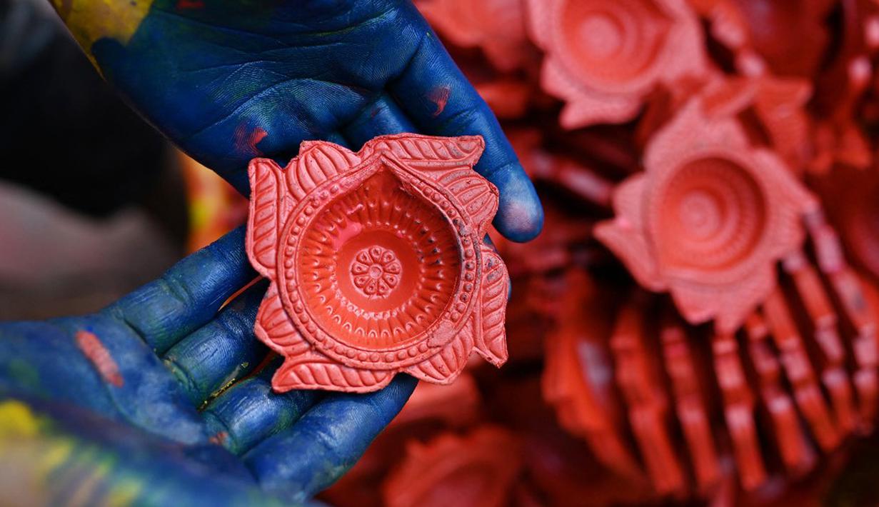 Seorang pembuat tembikar menunjukkan lampu tanah jelang Festival Diwali di sepanjang pinggir jalan di New Delhi, India, 18 Oktober 2022. Festival Diwali atau dalam agama Hindu berarti Festival Cahaya melambangkan kemenangan baik atas keburukan, dan lampu atau pelita dinyalakan sebagai tanda perayaan serta harapan umat manusia. (Sajjad HUSSAIN/AFP)