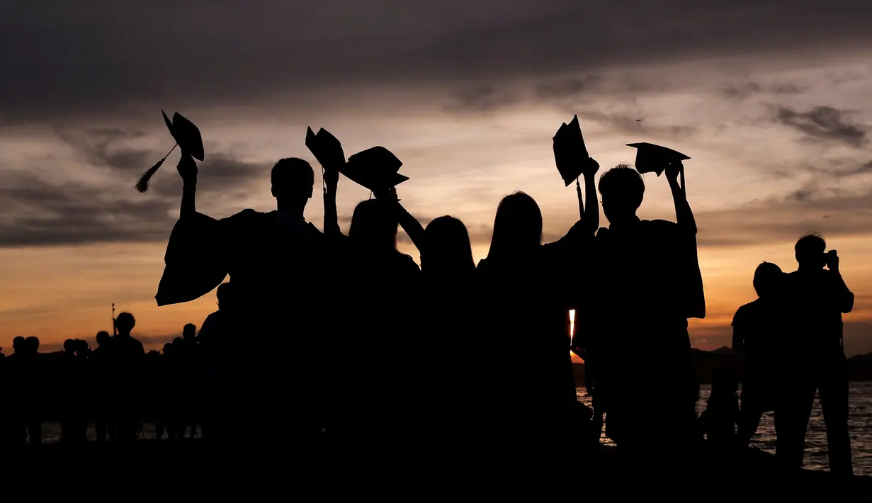 Siswa yang mengenakan gaun kelulusan mereka berpose untuk foto saat matahari terbenam di Victoria Harbour, Hong Kong, Selasa (30/6/2020). (AP Photo/Kin Cheung)
