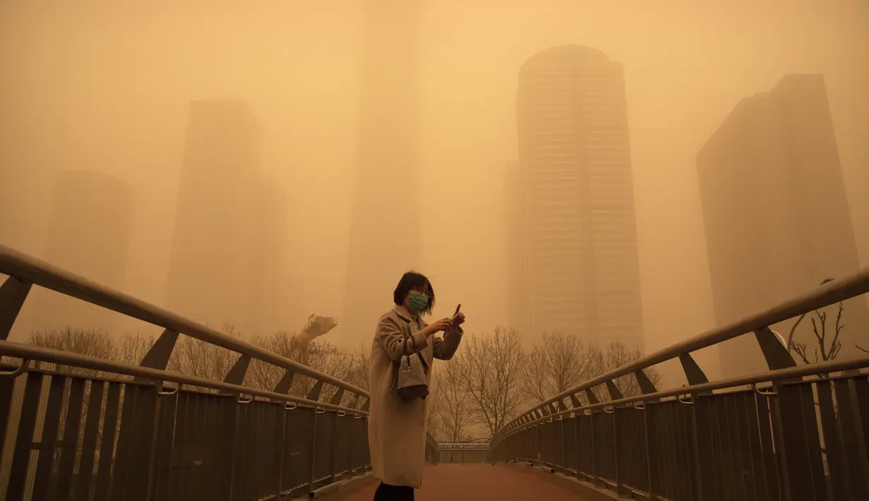 Seorang perempuan berjalan di sepanjang jembatan penyeberangan di tengah badai pasir pada jam sibuk pagi hari di kawasan pusat bisnis di Beijing, China, Senin (15/3/2021). Kota Beijing diselimuti debu cokelat tebal, Senin pagi, yang dibawa angin kencang dari Mongolia. (AP Photo/Mark Schiefelbein)