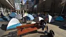 Seorang pria memakai sepatu di depan perkampungan tenda para tunawisma di kawasan Martin Place, pusat kota Sydney, 2 Agustus 2017. Pemerintah New South Wales menegaskan pihaknya akan menutup perkampungan tenda para tunawisma itu. (PETER PARKS / AFP)