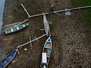 Seorang warga berjalan di samping perahu di hamparan Sungai Solimoes yang kering, akibat suhu tinggi yang melanda wilayah kota Manaquiri, di daerah pedesaan negara bagian Amazonas, Brasil, Sabtu, 21 Oktober 2023. (AP Photo/Edmar Barros)