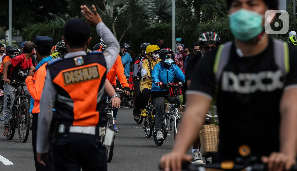Petugas mengatur lalu lintas saat warga bersepeda di kawasan Thamrin, Jakarta Pusat, Minggu (15/11/2020). Di masa PSBB transisi Jakarta, warga tetap melakukan aktivitas olahraga, khususnya bersepeda yang kini banyak diminati bahkan menjadi tren. . (Liputan6.com/Johan Tallo)