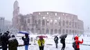 Sejumlah wisatawan mengabadikan Colosseum kuno saat hujan salju di Roma, Italia (26/2). (AFP Photo/Vicenzo Pinto)