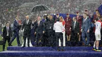 Presiden Rusia, Vladimir Putin dilindungi oleh seorang pemandu yang memegang payung sementara para pejabat lainnya basah kuyup saat hujan turun selama penyerahan medali dan trofi Piala Dunia 2018 di Stadion Luzhniki, Minggu (15/7). (AP/Matthias Schrader)