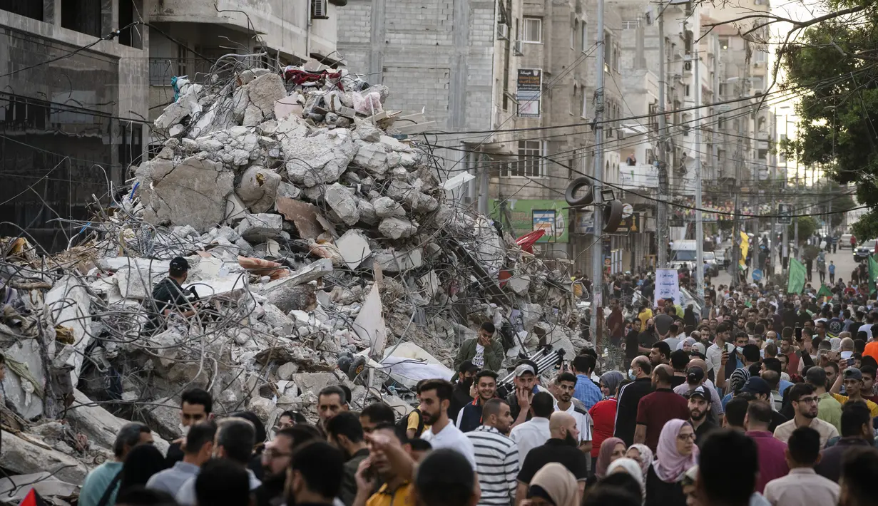Orang-orang melewati tumpukan puing di samping bangunan yang hancur oleh serangan udara Israel, di Kota Gaza, Jumat (21/5/2021). Israel dan Hamas telah sepakat untuk gencatan senjata di Jalur Gaza setelah 11 hari pertempuran. (AP Photo/John Minchillo)