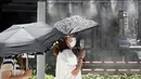 Seorang wanita mengenakan masker wajah untuk membantu melindungi dari penyebaran virus corona menggunakan kipas angin portabel di dekat titik kabut pendingin di sebuah jalan di Tokyo, Selasa (10/8/2021). (AP Photo/Eugene Hoshiko)
