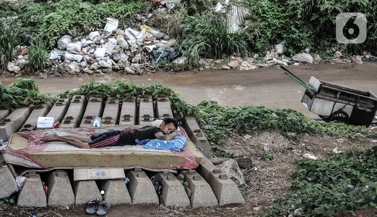 Seorang tunawisma tidur di lapaknya di kolong rel dwi ganda atau double-double track (DDT), kawasan Manggarai, Jakarta, Kamis (7/1/2021). Mereka yang terpaksa berprofesi sebagai pemulung memilih tinggal di sana akibat ketimpangan sosial yang semakin tinggi di Ibu Kota. (merdeka.com/Iqbal S. Nugroho)