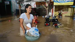 Seorang ibu membawa anaknya menggunakan ember untuk melintasi banjir di kabupaten Bandung, Jawa Barat, Minggu (13/3). Kawasan Bandung Selatan kembali dilanda banjir akibat luapan Sungai Citarum dan membuat ribuan orang mengungsi. (Timur Matahari/AFP)