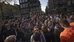Seorang pria membawa sepedanya bergerak di antara kerumunan warga yang merayakan Hari Raja di pusat Kta Amsterdam, Belanda, Selasa (27/4/2021). Warga berkumpul di kota-kota seluruh Belanda untuk menandai ulang tahun Raja Willem-Alexander. (AP Photo/Peter Dejong)