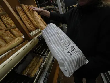 Pemilik toko roti Florence Poirier memasukkan baguette ke dalam kantong untuk pelanggan di toko roti, di Versailles, sebelah barat Paris, Selasa, 29 November 2022.  Baguette Prancis resmi diberi status warisan budaya takbenda UNESCO pada Rabu, 30 November 2022. (AP Photo/Michel Euler)