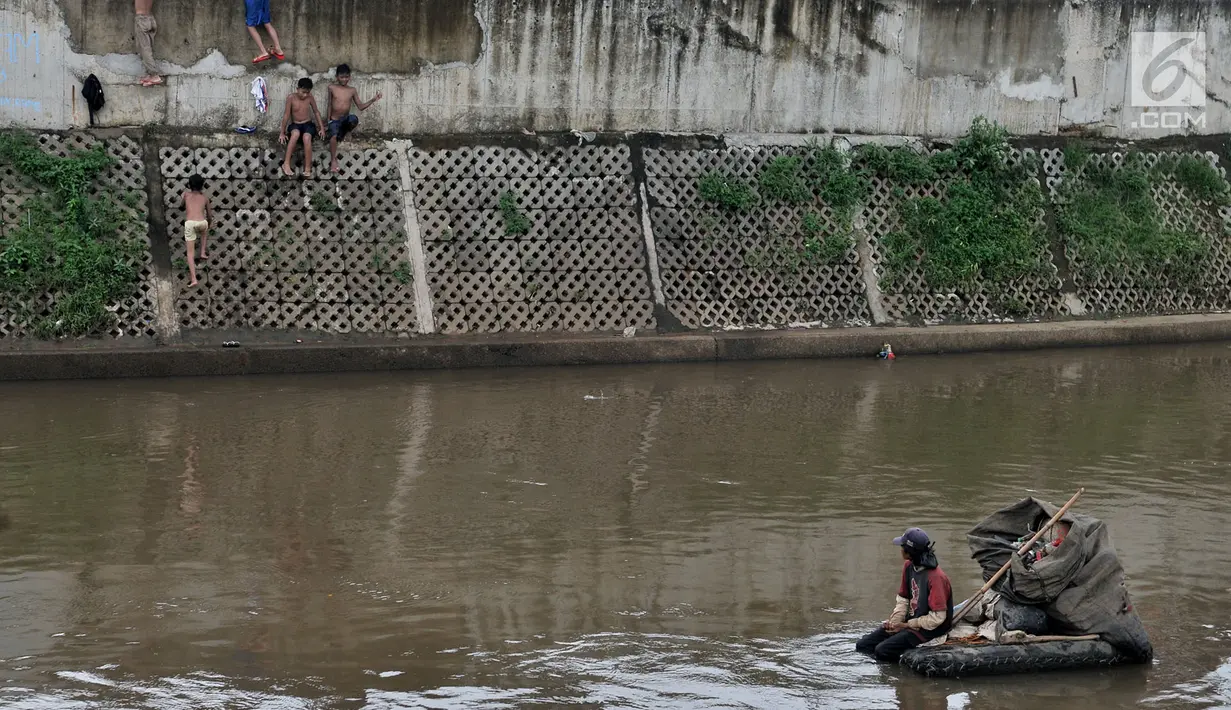 Pencari barang bekas melihat anak-anak yang sedang bermain di Kali Ciliwung, Kampung Pulo, Jakarta, Minggu (27/1). Keterbatasan ekonomi menjadikan Kali Ciliwung sebagai tempat bermain bagi anak-anak menghabiskan libur sekolah.(Merdeka.com/Iqbal Nugroho)