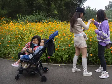 Seorang wanita berfoto dengan seorang anak di dekat bunga yang mekar di taman umum di Beijing, Sabtu (2/10/2021). Pengunjung memadati taman dan lokasi wisata di Beijing saat China merayakan hari kedua masa libur Hari Nasional. (AP Photo/Mark Schiefelbein)