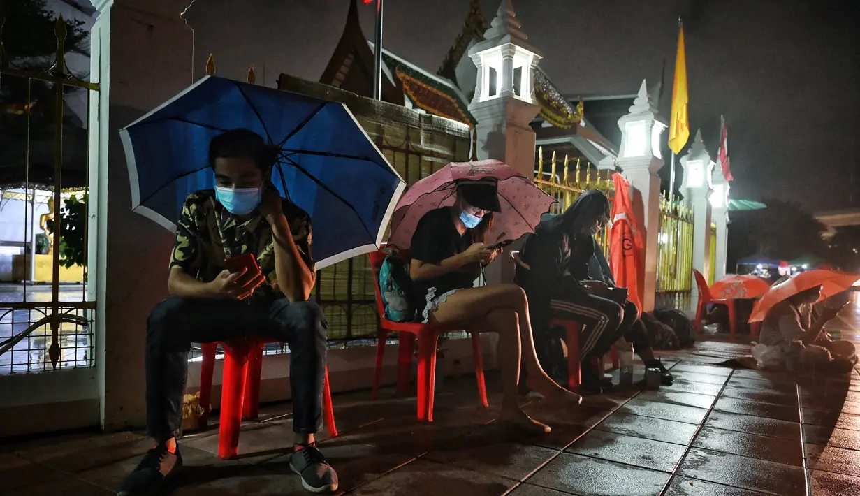 Orang-orang menggunakan ponsel mereka saat antre semalaman untuk tes swab Covid-19 gratis di Wat Phra Sri Mahathat Woramahawihan di Bangkok, Jumat (9/7/2021) dinihari. Thailand pada Kamis (8/7/2021), mencatat rekor 75 kematian Covid-19 dalam 24 jam terakhir. (Lillian SUWANRUMPHA/AFP)