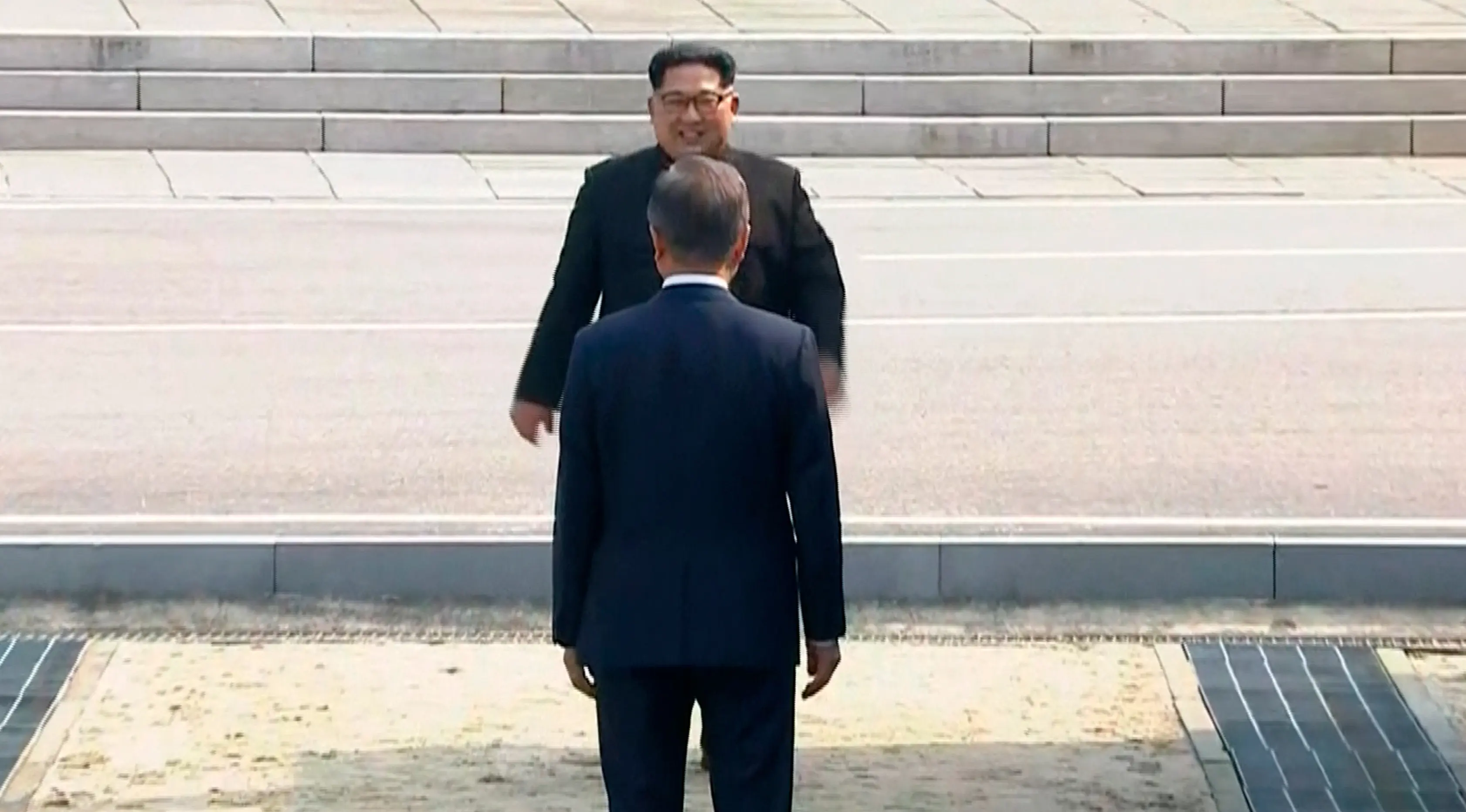 Presiden Korea Selatan, Moon Jae-in menyambut kedatangan Pemimpin Korea Utara, Kim Jong-un di Zona Demiliterisasi (DMZ), Panmunjom, Jumat (27/4). Keduanya berjabat tangan sambil menempatkan senyum di bibir masing-masing. (Korea Broadcasting System via AP)