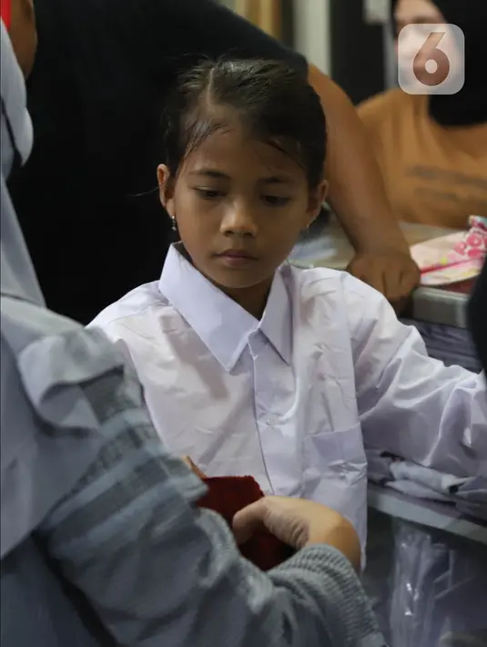 Calon pembeli mencoba seragam sekolah kepada anaknya di Pasar Kebayoran Lama, Jakarta, Jumat (8/7/2022). Menjelang dimulainya tahun ajaran baru, para orang tua disibukkan berbelanja baju seragam dan perlengkapan sekolah untuk anak mereka. (Liputan6.com/Angga Yuniar)