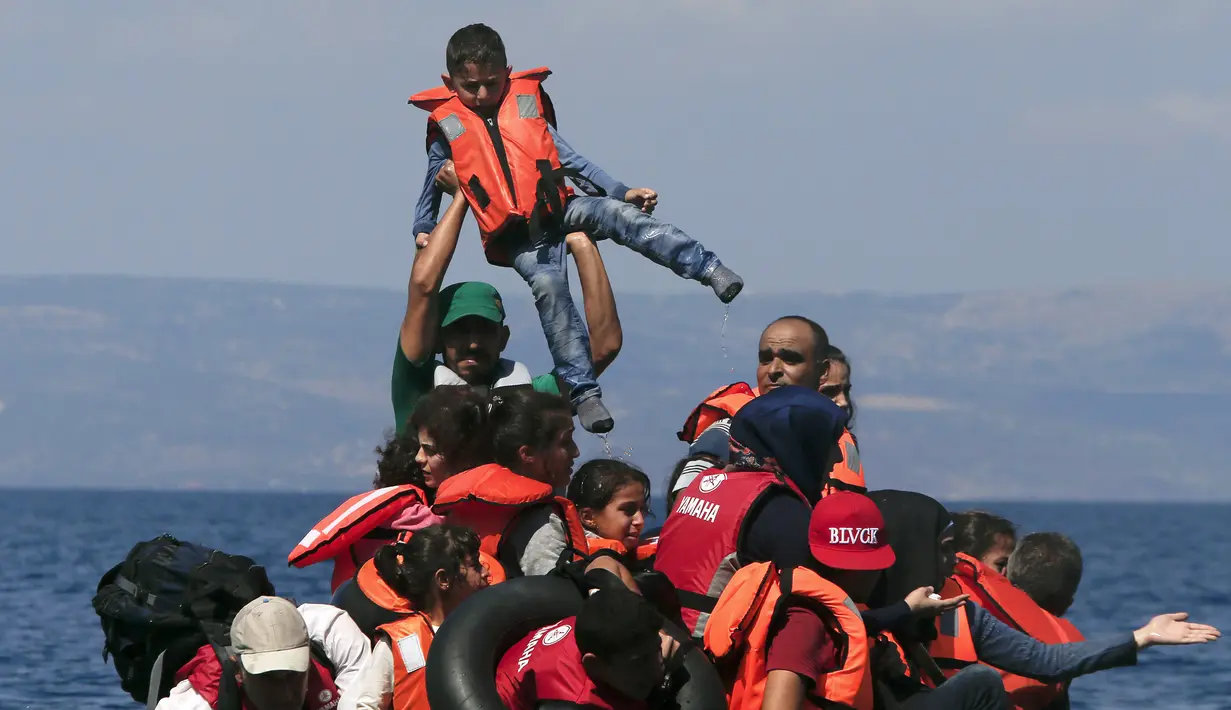 Seorang anak diangkat oleh salah satu pengungsi Suriah saat perahu karet yang mereka tumpangi bocor sekitar 100 m sebelum mencapai pulau Lesbon, Yunani, Minggu (13/09/2015). (REUTERS/Alkis Konstantinidis)