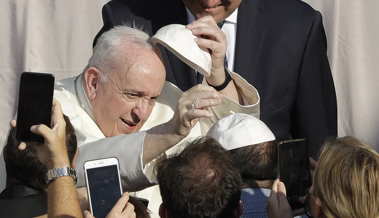 Paus Fransiskus menukar topi yang disumbangkan oleh umat saat ia tiba di halaman St. Damaso pada kesempatan audiensi umum mingguan di Vatikan, Rabu (16/9/2020). (AP Photo/Gregorio Borgia)