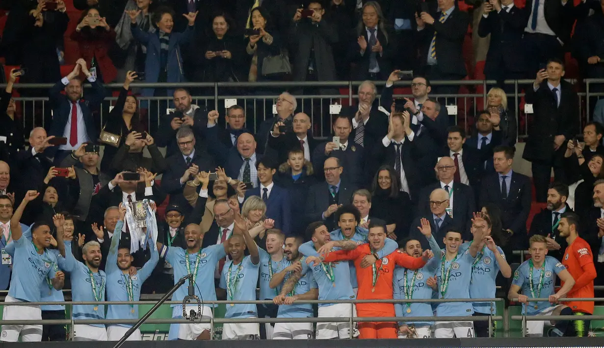 Pemain Manchester City mengangkat trofi setelah memenangkan pertandingan final Piala Liga Inggris melawan Chelsea di Wembley, Minggu (24/2). Manchester City dipaksa bertarung hingga babak adu penalti untuk mengandaskan perlawanan Chelsea. (AP Tim Ireland)