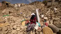 Seorang wanita duduk di samping barang-barang yang bisa diselamatkan di tengah reruntuhan di desa Douzrou yang dilanda gempa bumi di provinsi al-Haouz di pegunungan Atlas Tinggi di Maroko tengah pada 12 September 2023. (FADEL SENNA/AFP)