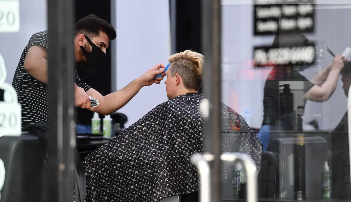 Seorang penata rambut yang mengenakan masker melayani pelanggan di Central Business District (CBD) Melbourne, Negara Bagian Victoria, Australia, 19 Oktober 2020. PM Australia Scott Morrison merilis pernyataan guna menyambut pelonggaran lockdown secara parsial di Victoria. (Xinhua/Bai Xue)