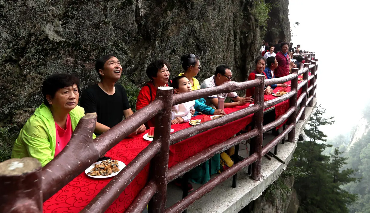 Wisatawan menyantap makanan pada acara perjamuan di sepanjang tepi tebing di Laojun Mountain provinsi Henan, China. Wisatawan menikmati berbagai suguhan makanan di jalanan selebar enam kaki yang menempel pada tebing setinggi 2.000 meter. (AFP)
