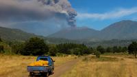 Mobil berjalan saat Gunung Raung mengeluarkan awan panas yang terlihat dari Kabupaten  Bondowoso, Jatim, Minggu (12/7). Gunung Raung terus menunjukkan aktivitas vulkaniknya dan menyebabkan terjadi hujan abu tipis di sejumlah wilayah. (AFP PHOTO/WIDARSHA)