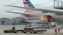 Api berkobar di landasan Bandara Internasional Hong Kong, dekat dengan lambung pesawat American Airlines yang terparkir untuk memuat barang, Senin (9/10). Menurut keterangan, benda yang terbakar itu merupakan mobil pengangkut barang bawaan. (U87 via AP)