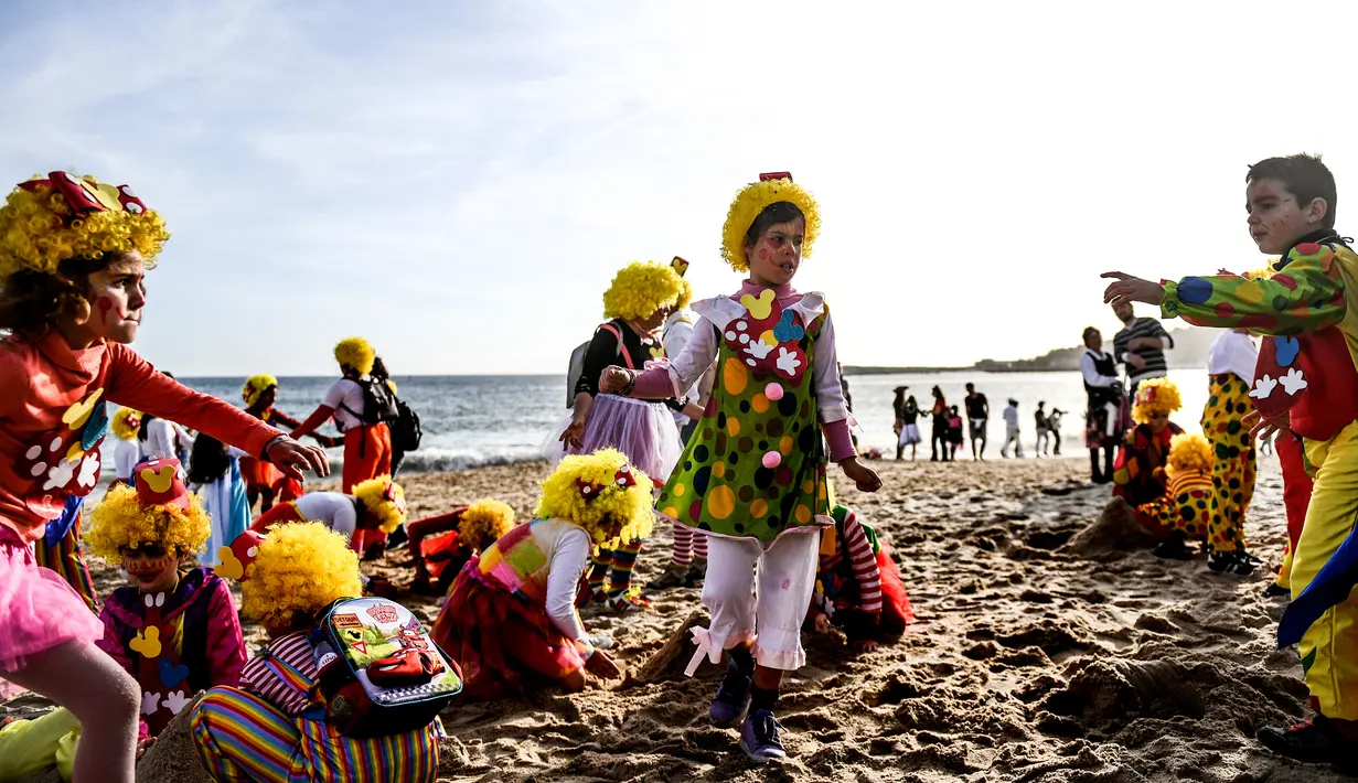Anak-anak dengan pakaian badut bermain di pantai selama parade badut tahunan di Sesimbra, Portugal pada Senin (4/3/2019). Tidak hanya orang dewasa anak-anak pun ikut merias diri menjadi badut. (PATRICIA DE MELO MOREIRA / AFP)