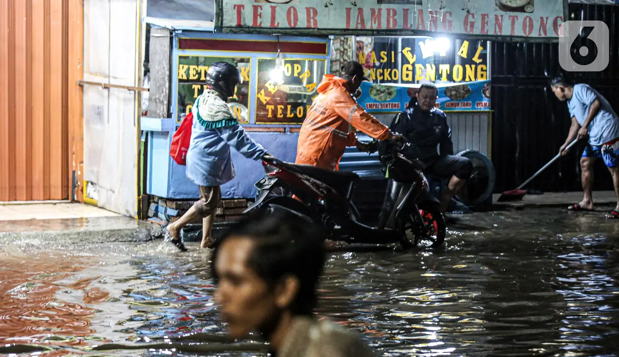 Pengendara sepeda motor mendorong kendaraannya saat melewati banjir di Jalan Ciracas Raya, Jakarta, Jumat (12/8/2022). Hujan lebat yang terjadi sore tadi membuat Jalan Ciracas Raya tergenang air dan kendaraan terjebak banjir. (Liputan6.com/Faizal Fanani)