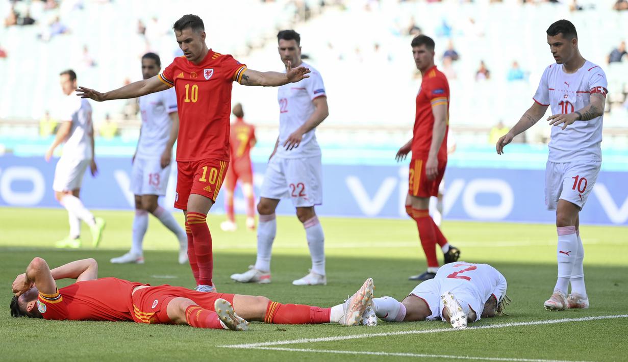 Usai melepaskan sundulan, Kieffer Moore (kiri) terlibat benturan kepala dengan bek Swiss, Kevin Mbabu. Keduanya tergeletak akibat insiden tersebut. (Foto: AP/Dan Mullan/Pool)
