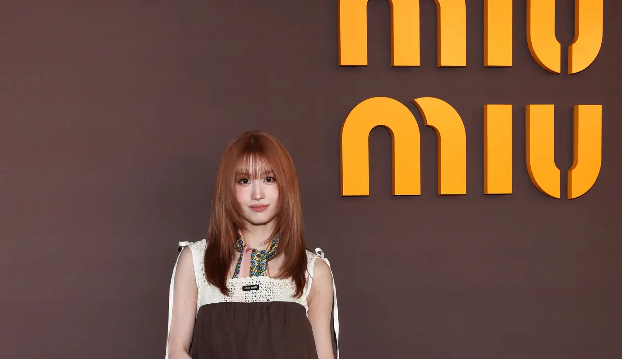 Momo TWICE tampil dengan gaya playful bernuansa vintage. Ia mengenakan mini dress cokelat bersiluet babydoll yang dipadukan dengan panel rajut krem pada bagian atas. Aksen scarf bermotif warna-warni di leher menambah sentuhan retro yang khas. [Dok/Miu Miu].