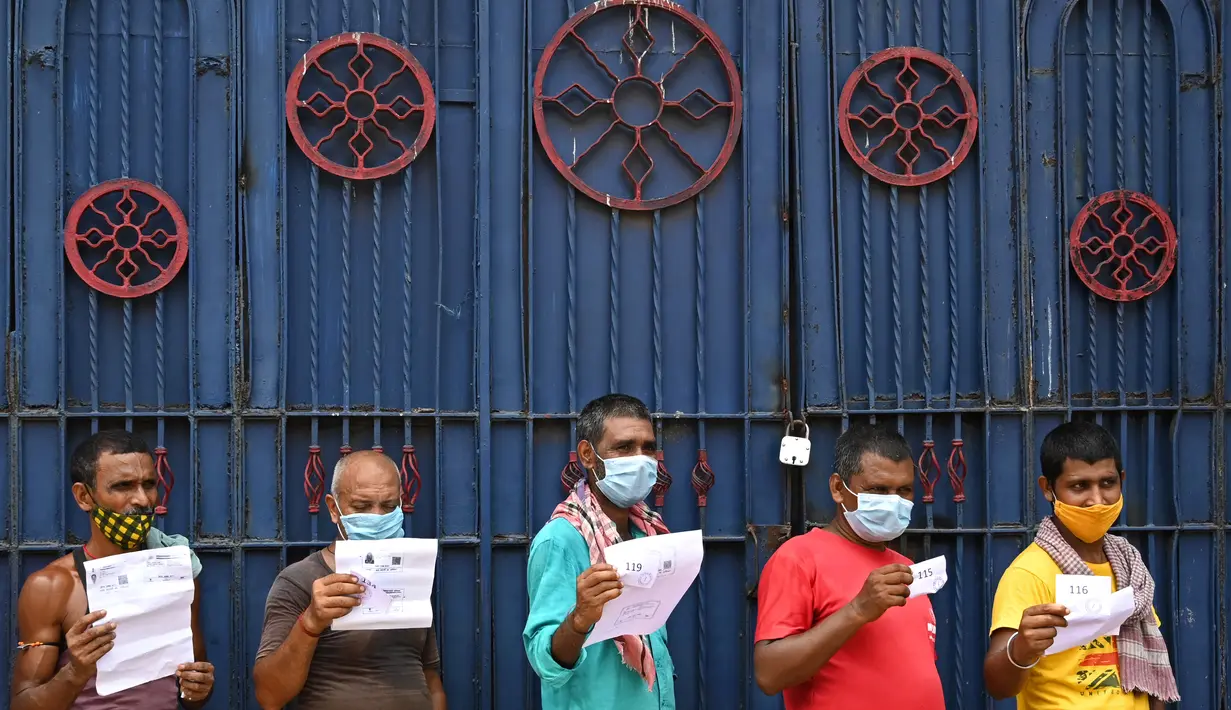 Pekerja memegang dokumen saat menunggu giliran menerima vaksin Covid-19 Covishield di dalam bus penumpang yang diubah menjadi pusat vaksinasi keliling di Kolkata, Kamis (3/6/2021). India telah menderita pandemi yang menghancurkan sejak April, dan baru-baru ini mulai mereda. (Dibyangshu SARKAR/AFP)