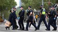 Orang-orang membawa belanjaan mereka saat polisi berpatroli di Melbourne, Australia, Kamis (30/9/2021). Melbourne bergulat dengan lonjakan infeksi Covid-19 di mana sebanyak 1.438 kasus dilaporkan, jumlah harian terbesar sejak awal pandemi. (William WEST / AFP)