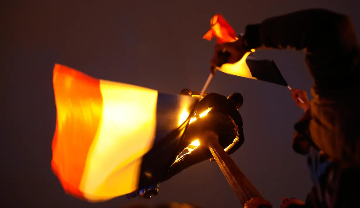 Seorang pria memanjat lampu jalan sambil membawa bendera Prancis di luar museum Louvre, Paris, Minggu (7/5). Ratusan pendukung Emmanuel Macron menyambut kemenangan kandidat termuda yang terpilih sebagai presiden negeri itu . (AP Photo/Laurent Cipriani)