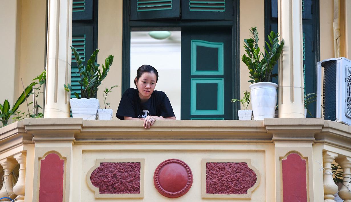 Gambar pada 3 September 2021 menunjukkan seorang perempuan melihat keluar dari balkon rumahnya di Hanoi, Vietnam, selama lockdown Covid-19. Menghadap ke jalan yang sepi, balkon kecil mereka menjadi saksi bisu terkait aktivitas yang dilakukan oleh masing-masing keluarga. (Nhac NGUYEN/AFP)