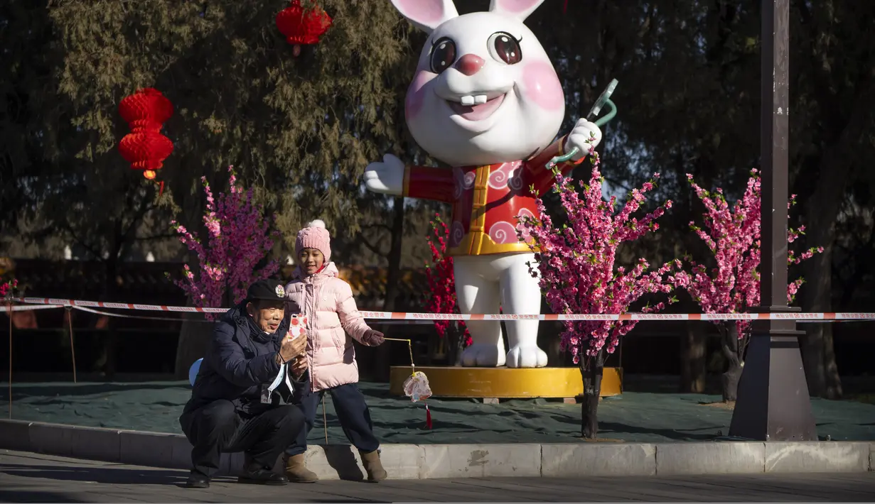Seorang pria dan wanita berpose untuk selfie di depan patung kelinci untuk Tahun Baru Imlek mendatang di sebuah taman umum di Beijing, Jumat, 20 Januari 2023. Berbagai hiasan dan pernak-pernik mulai menghiasi Taman di Beijing menjelang perayaan Tahun Baru Imlek. (AP Photo/Mark Schiefelbein)