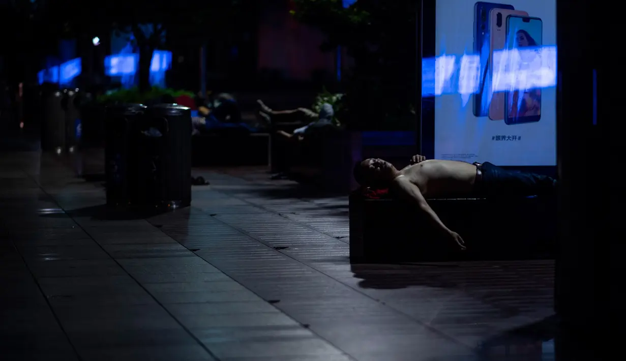 Sejumlah orang tidur bangku di sepanjang Nanjing East Road, Shanghai (8/8). Penduduk setempat mencari cara untuk menjaga tagihan listrik yang meroket selama musim panas. (AFP Photo/Johannes Eisele)