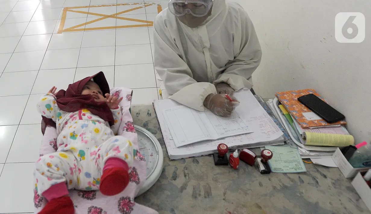 Petugas Kesehatan dengan Alat Pelindung Diri menimbang bayi di Rumah Vaksinasi Sawangan, Depok, Selasa (16/6/2020). Orang tua diminta tidak menunda pemberian imunisasi pada anak-anak yang masih harus menerima imunisasi lengkap, meskipun pandemi Covid-19 belum berakhir. (merdeka.com/Arie Basuki)