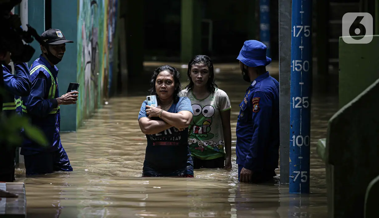 Warga berjalan melintasi banjir di kawasan Kampung Melayu, Jakarta, Senin (8/11/2021). Banjir akibat luapan Kali Ciliwung tersebut merendam pemukiman setinggi 60 cm sejak 7 November 2021 sore. (Liputan6.com/Faizal Fanani)