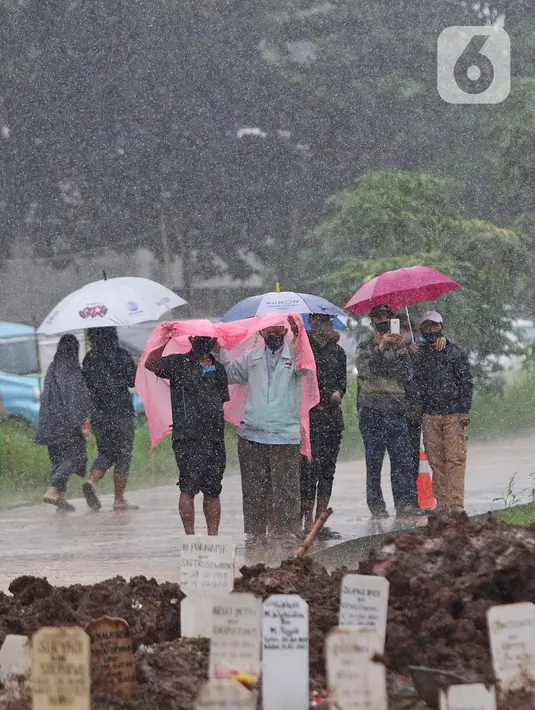 Keluarga dan kerabat jenazah kasus COVID-19 menyaksikan proses pemakaman di TPU Bambu Apus, Jakarta Timur, Selasa (16/2/2021). Pemangkasan petak makam di TPU Bambu Apus tersebut dilakukan agar bisa menampung lebih banyak jenazah, mengingat lahan pemakaman terbatas. (Liputan6.com/Herman Zakharia)