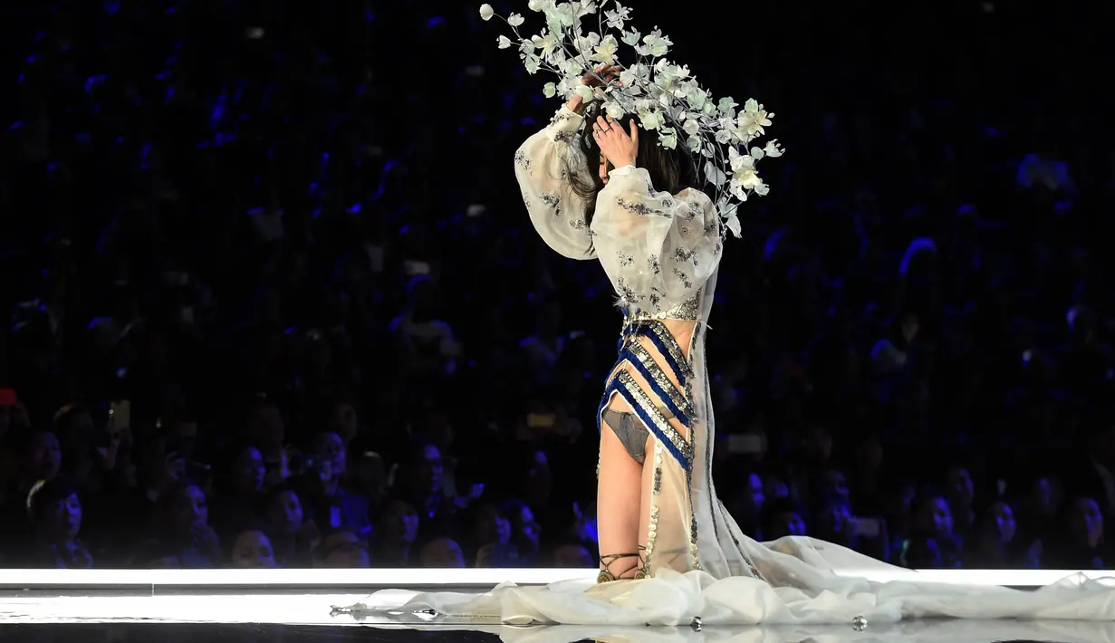 Model Tiongkok, Ming Xi terduduk di atas catwalk sambil memegangi headpiece bunga di kepalanya setelah terjatuh di atas catwalk Victoria’s Secret Fashion Show 2017 di Shanghai, Senin (20/11). Tampak wajah putih Ming menahan malu. (FRED DUFOUR/AFP)
