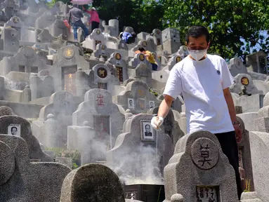 Seorang pria yang mengenakan masker membakar uang kertas di makam kerabat saat Festival Ching Ming atau Hari Sapu Makam di Hong Kong, Selasa (5/4/2022). Ribuan warga Hong Kong memberi hormat kepada leluhur dan kerabat mereka selama festival tahunan ini. (AP Photo/Vincent Yu)