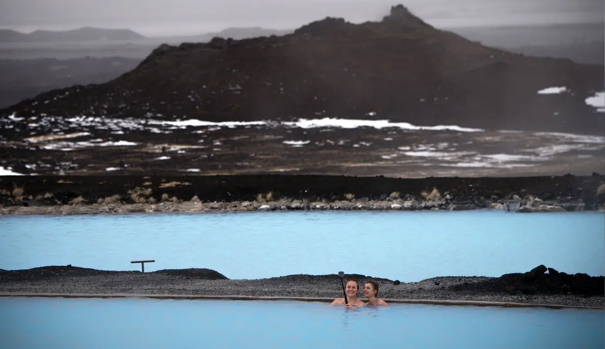 Dua wanita berselfie saat mereka berenang di sumber air panas di Myvatn, Islandia (12/4). Myvatn adalah danau eutrophic dangkal yang terletak di daerah vulkanisme aktif di utara Islandia, tidak jauh dari gunung berapi Krafla. (AFP Photo/Loic Venance)