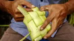 Seorang penjual menganyam daun kelapa atau kulit ketupat sambil menunggu pelanggan di sebuah pasar tradisional di Jakarta pada 2 April 2024. (BAY ISMOYO/AFP)