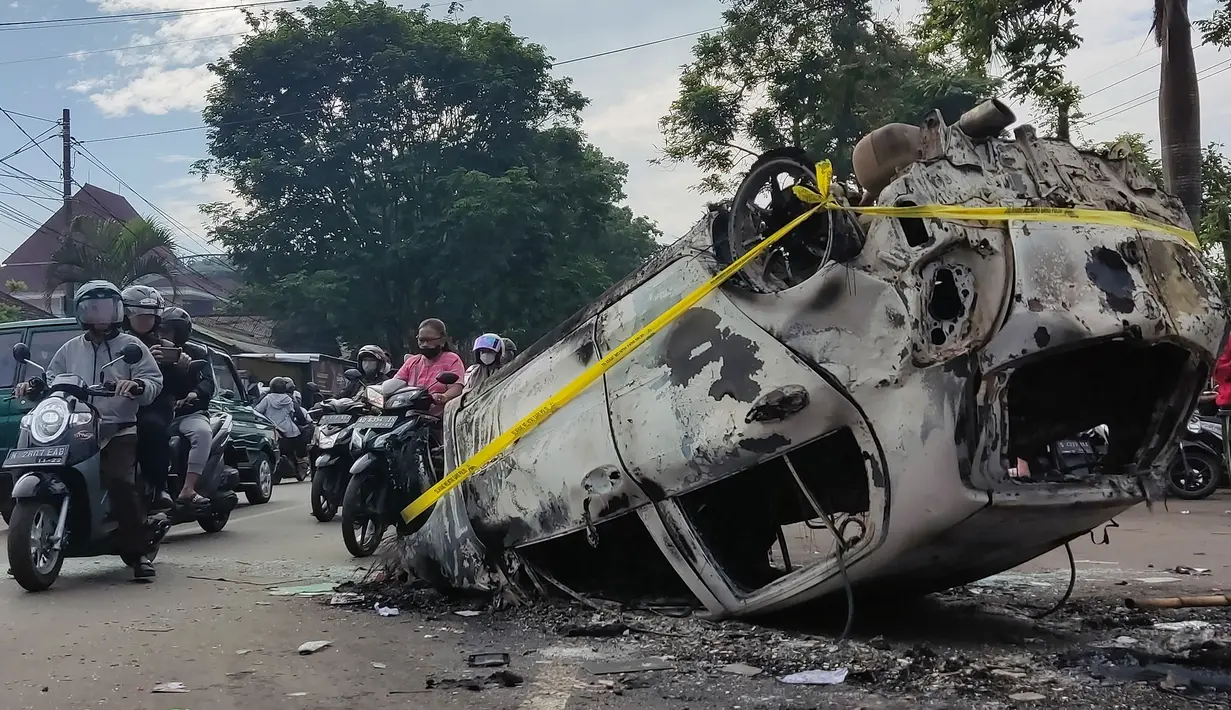 Pengendara melewati puing-puing mobil yang terbakar dalam kerusuhan di luar Stadion Kanjuruhan, Malang, Jawa Timur, Minggu (2/10/2022). Sebanyak 127 orang tewas ketika para penggemar yang marah menyerbu lapangan sepak bola setelah pertandingan antara Arema FC dan Persebaya Surabaya pada 1 Oktober 2022. (AP Photo/Hendra Permana)