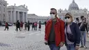 Pasangan mengenakan masker berjalan-jalan di luar Lapangan Santo Petrus, di Vatikan (27/2/2020). Pemerintah Italia akan melarang orang berciuman di tempat umum, berjabatan tangan dan menjaga jarak yang aman dari masing-masing lain untuk membatasi penyebaran virus corona. (AP Photo/Gregorio Borgia)